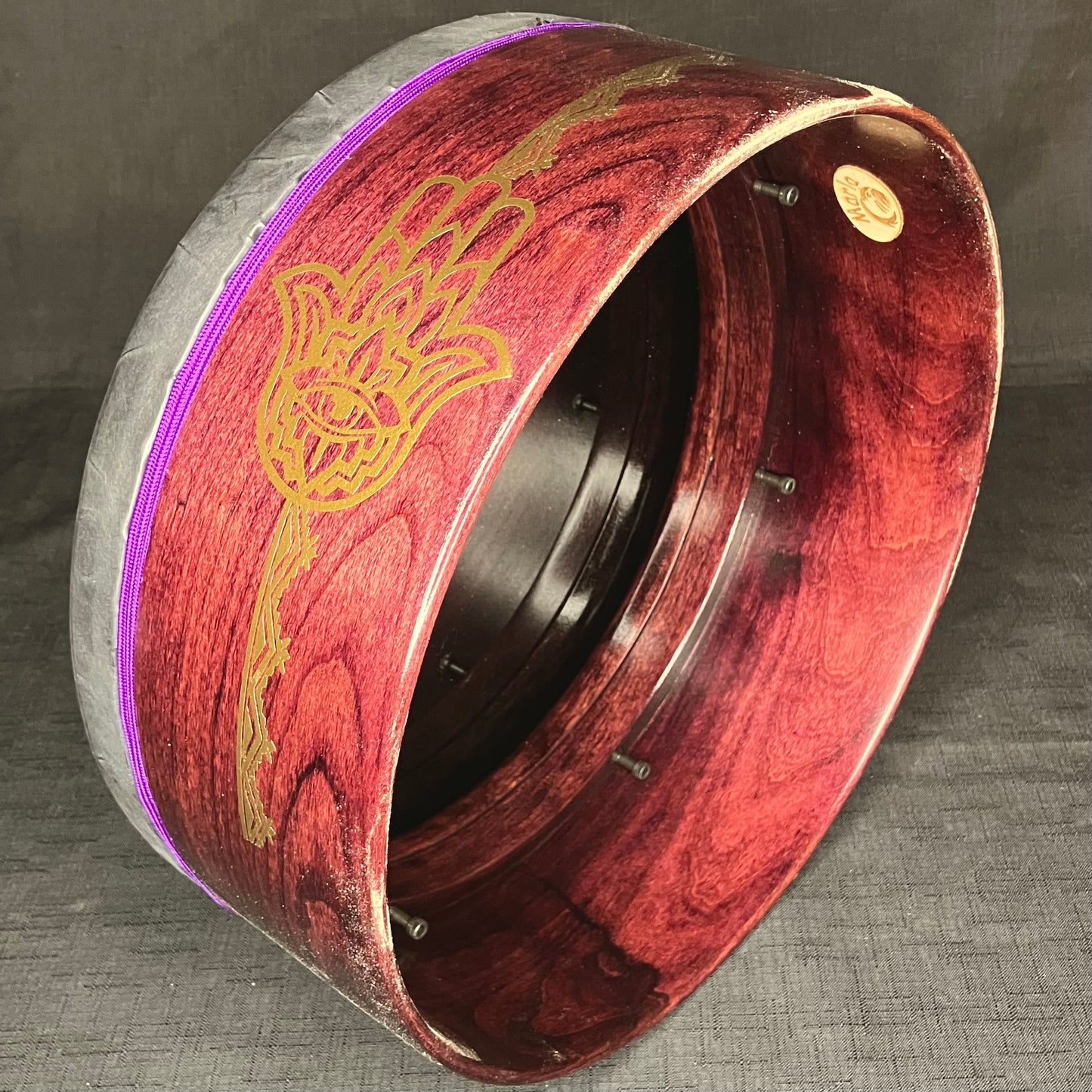 A handcrafted Cooperman drum with a dark purple-haze stain and decorative purple cording, featuring a thumb hole and a rolled bearing edge.