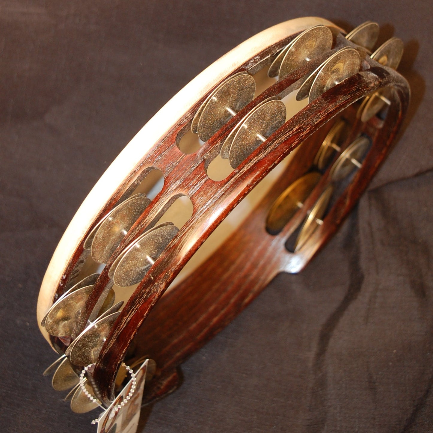 A processional tambourine with a wooden body and metal jingles, finished in clear lacquer and stained dark brown, held in an upright position.