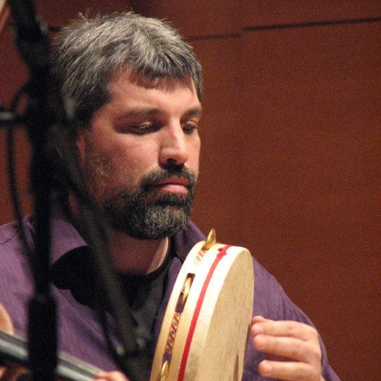 A person playing a Todd Roach Hybrid Tambourine with a natural, clear lacquer finish and decorative inlay, held vertically.