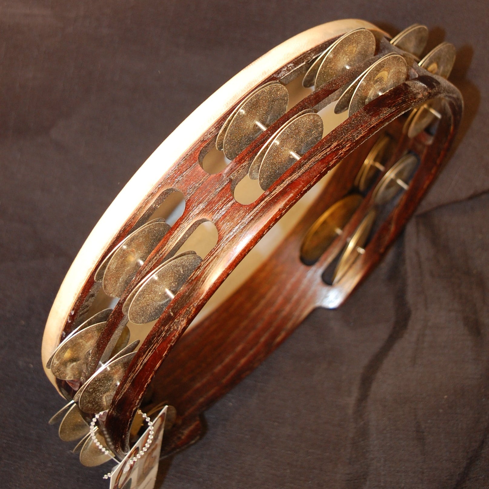 A processional tambourine with a wooden body and metal jingles, finished in clear lacquer and stained dark brown, held in an upright position.